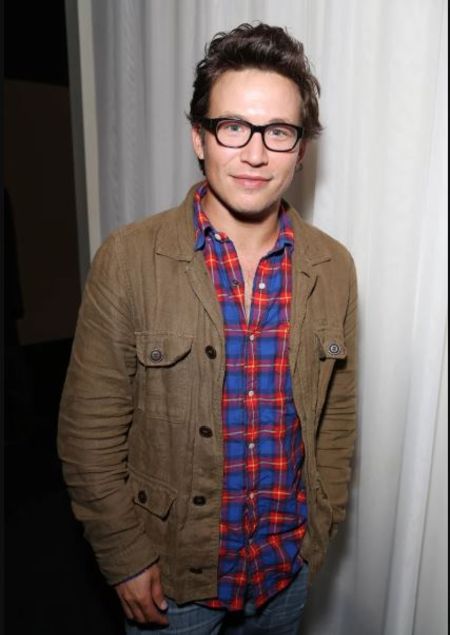 Actor Jonathan Taylor Thomas in a brown jacket poses for a picture.